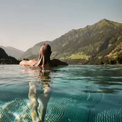 Eine Frau lehnt sich an den Rand vom Pool und schaut in die Berge.