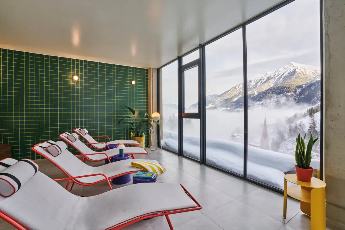 Spa-Bereich Urban Nature Badeschloss Bad gastein Mehere Liegen stehen vor einem Fenster mit Blick auf eine verschneite Berglandschaft.