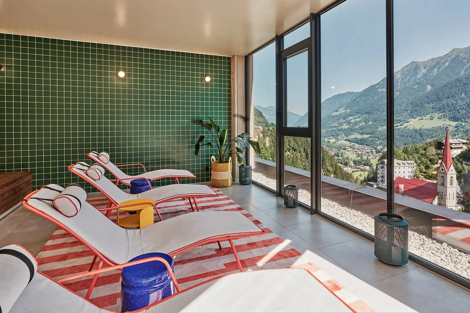 Ruheraum im Alpine Swim Club in Bad Gastein Moderner Ruheraum mit stylischen Liegen, großen Panoramafenstern und Blick auf die Berge und Kirche von Bad Gastein