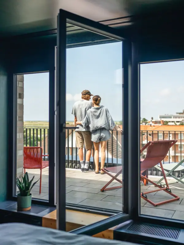Ausblick Balkon Ein Paar steht auf einem Balkon von einem Zimmer im Urban Nature Hotel St. Peter-Ording und blickt nach draußen.