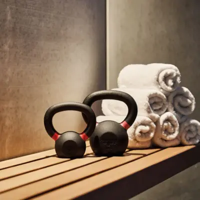 Zwei Kettlebells und mehrere aufgerollte Handtücher auf einer Holzbank in einem modernen Fitness- oder Wellnessbereich