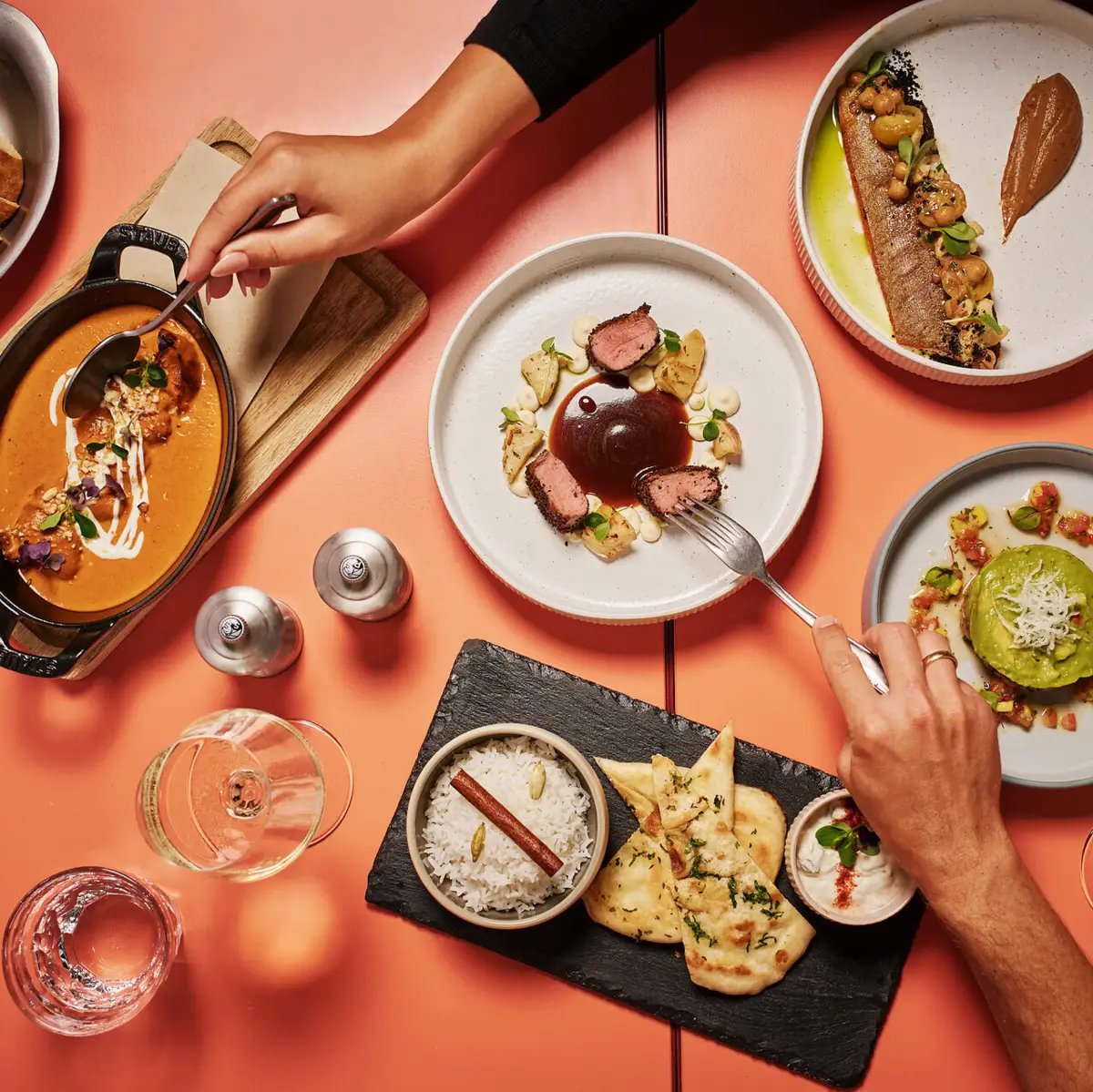 Bunte Auswahl an regionalen und mediterranen Spezialitäten auf einer orangenen Tischplatte mit Fleisch, Getränken und Vorspeisen