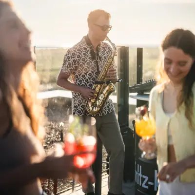 Die Rooftopbar Scraper's Club im Urban Nature Hotel St. Peter Ording mit einem Saxophon-Spieler und Menschen, die mit Getränken in der Hand tanzen.