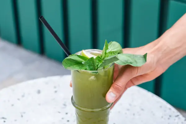 Eine Hand stellt eine grüne Limonade mit Basilikum auf einen Tisch.