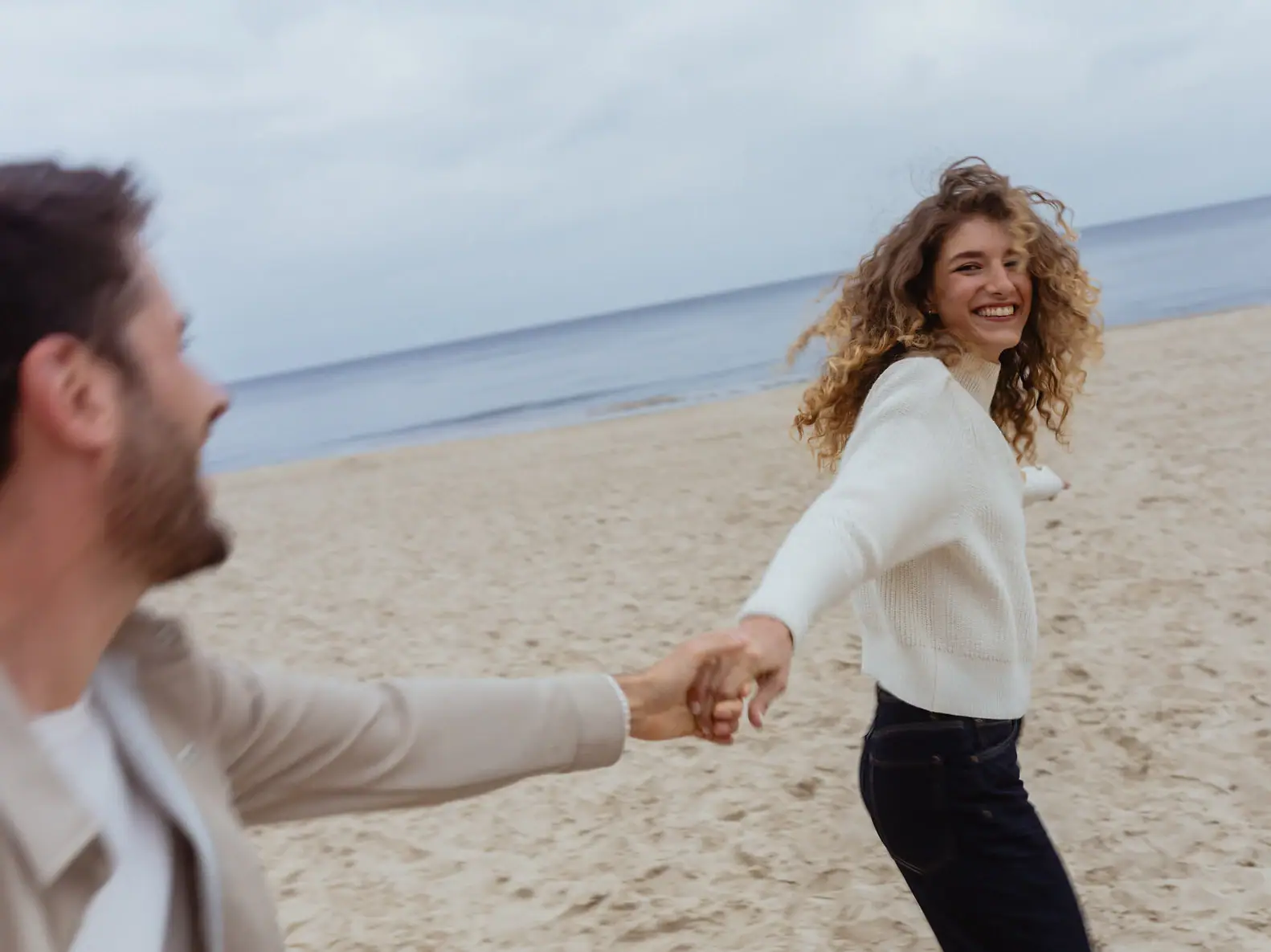 Eine Frau hält die Hand eines Mannes am Strand.