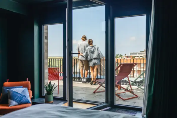 Ein Paar steht auf einem Balkon und schaut aus einem Fenster.