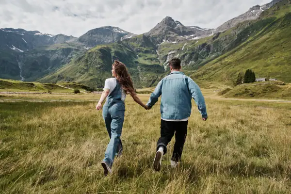 Ein Mann und eine Frau halten sich an den Händen in einem Feld mit Bergen im Hintergrund.